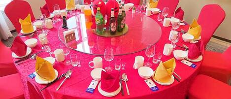 A round table with a glass top, surrounded by red chairs, set with plates, glasses, and cutlery.