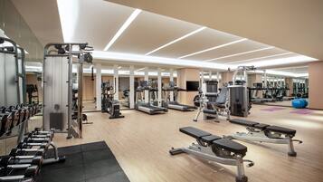A modern gym with various exercise equipment, mirrored walls, and a wooden floor.