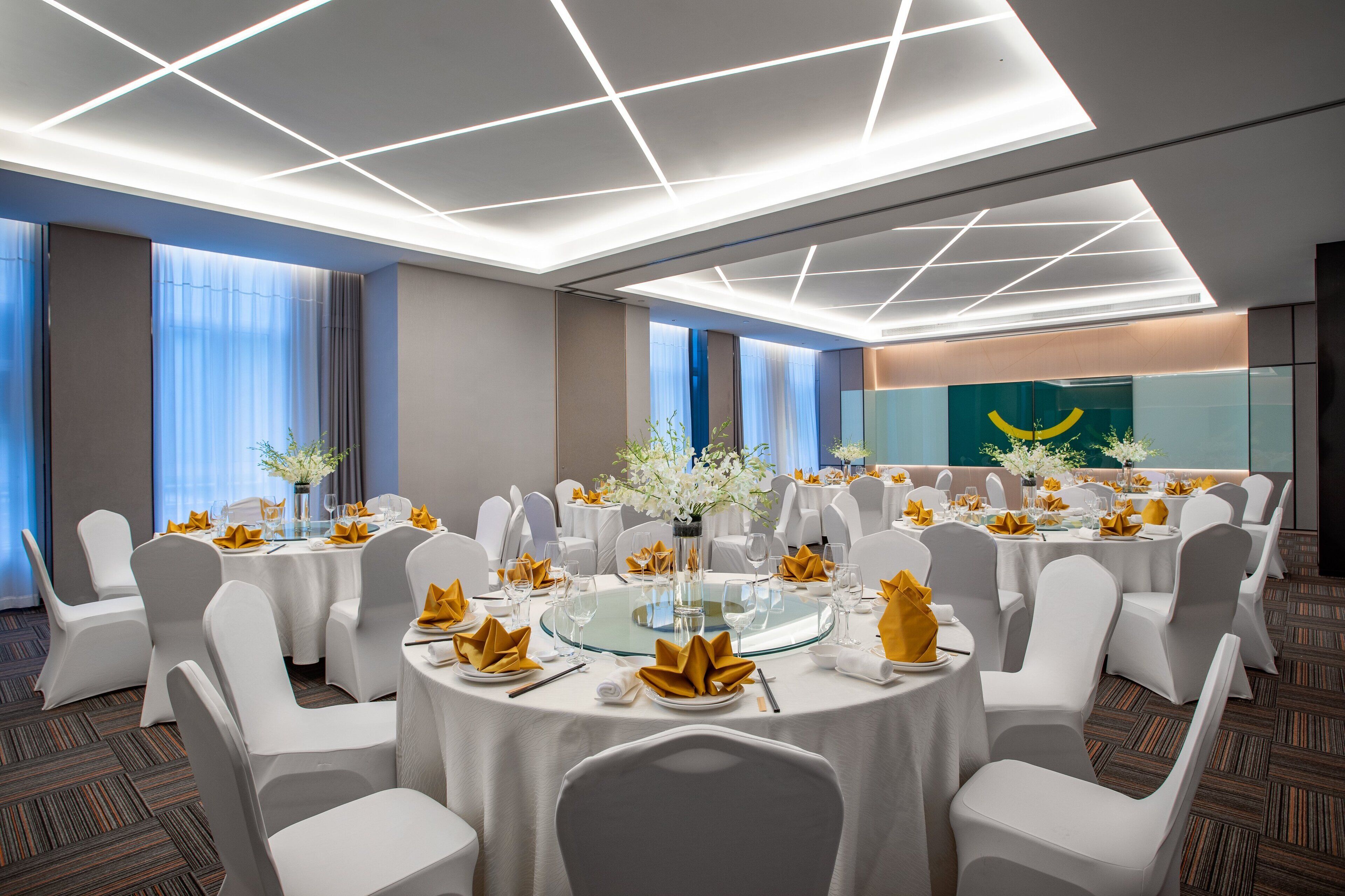 Un salón de conferencias con mesas redondas, sillas blancas y un centro de mesa de cristal.