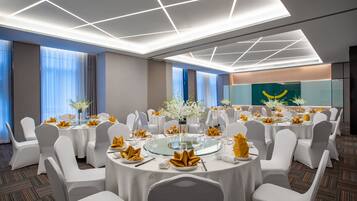 Un salón de conferencias con mesas redondas, sillas blancas y un centro de mesa de cristal.