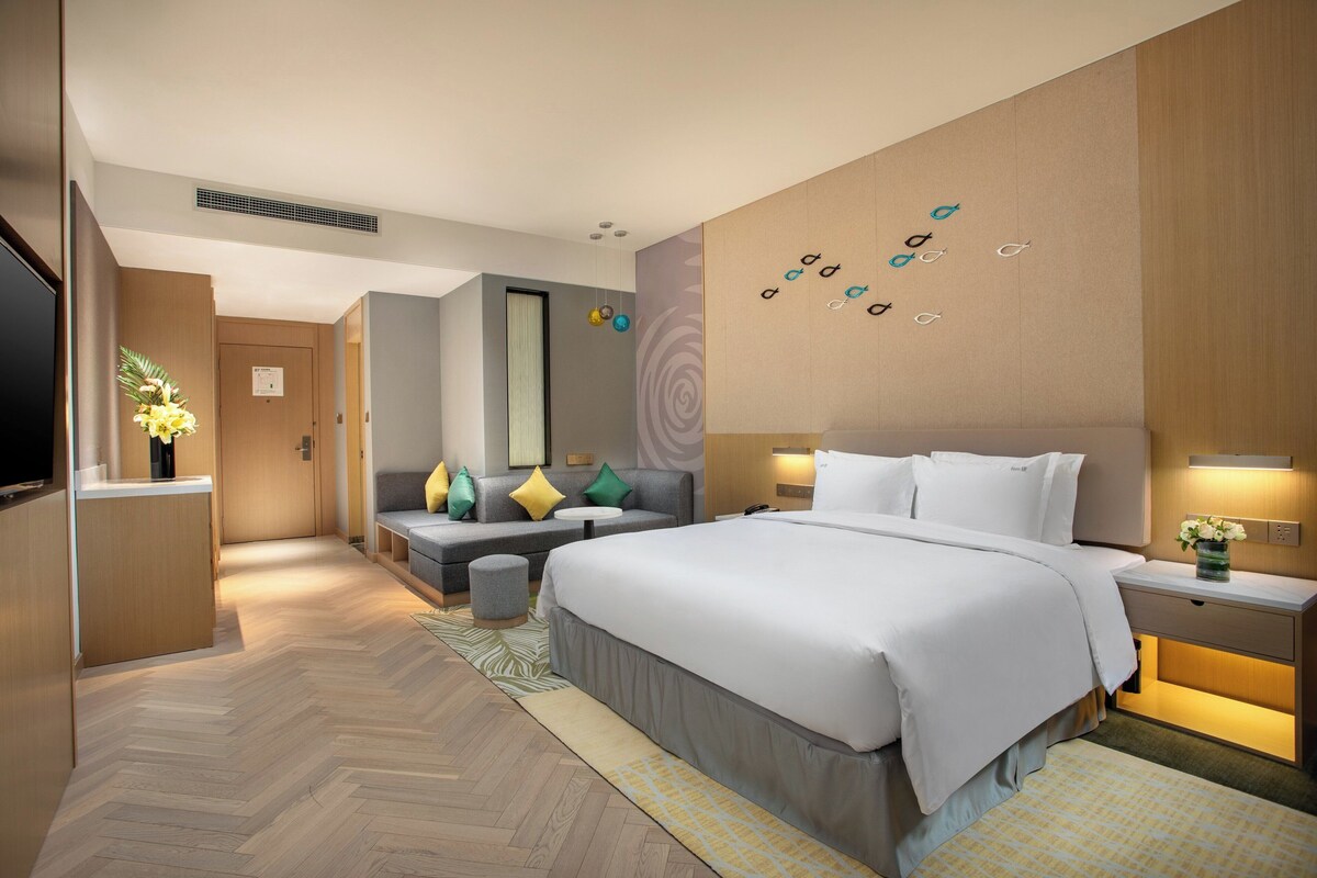 A modern hotel room with a large bed, a sofa, a desk, and a TV.