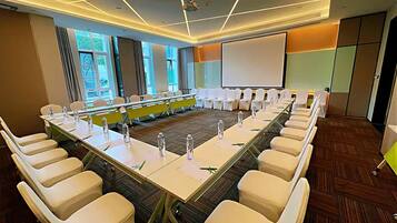 A conference room with a long table, white chairs, and a projector screen.