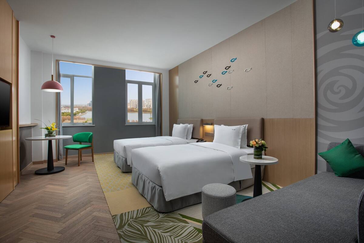 Ett hotellrum med två sängar, ett litet bord, en stol, en TV och utsikt över staden.