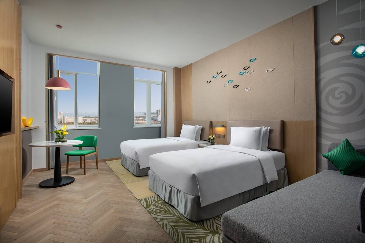 Ett hotellrum med två sängar, en matplats med bord och stolar, en TV och utsikt över staden.
