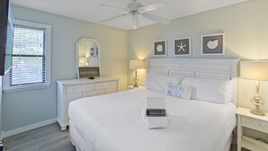Een keurig opgemaakt slaapkamer met een bed, een dressoir, een kaptafel, een plafondventilator en wanddecoratie.