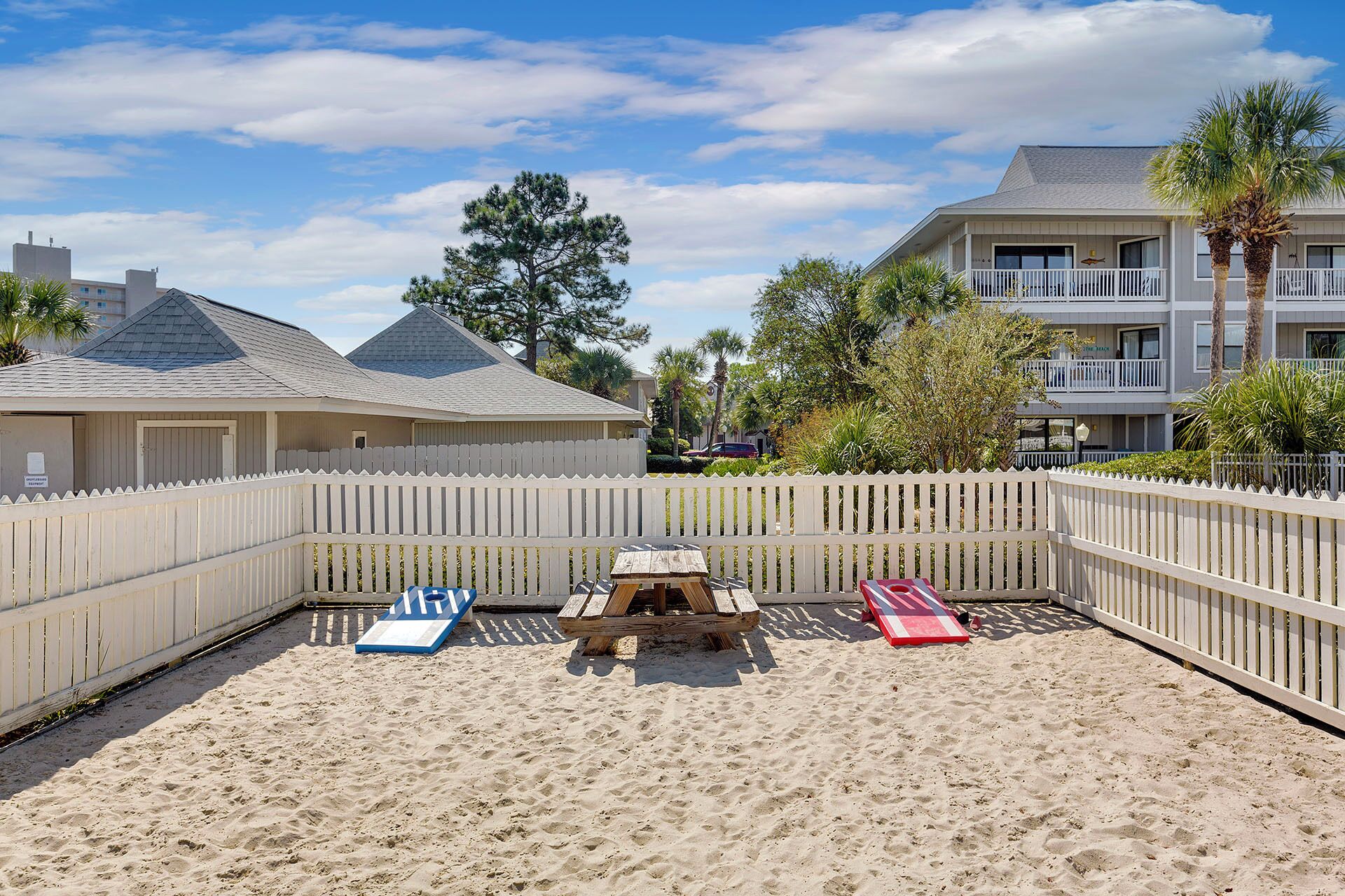 A beach area with a wooden fence, a picnic table, and lounge chairs.