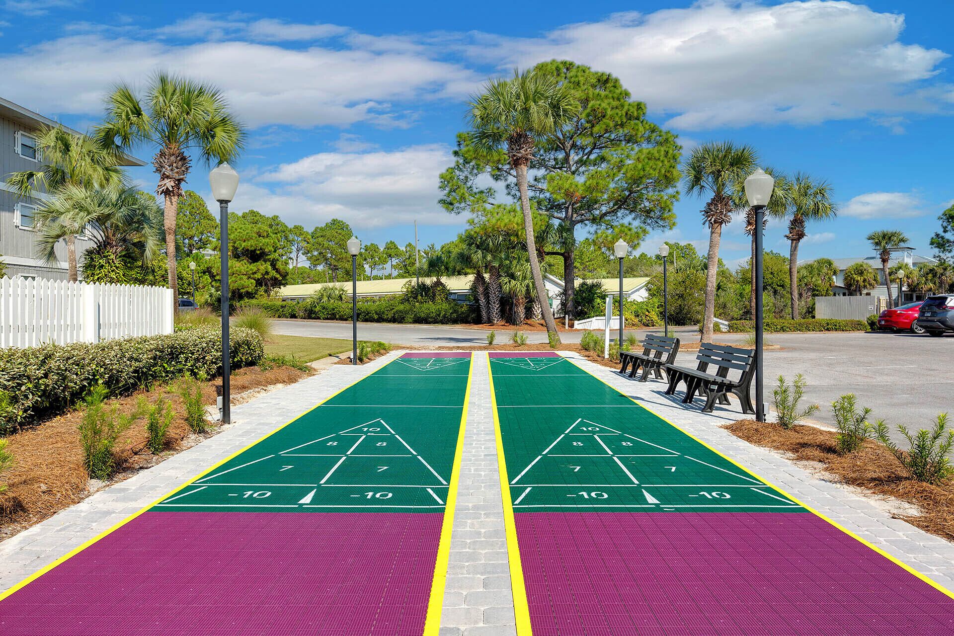 A shuffleboard court with green and purple lanes, benches, and palm trees.