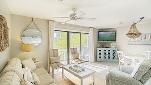 Een ruime woonkamer met een plafondventilator, een televisie en een eethoek met witte meubels.