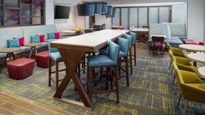 A modern hotel lobby with a long communal table, blue and red seating, and a patterned carpet. - Hampton Inn Kissimmee North (Kissimmee)