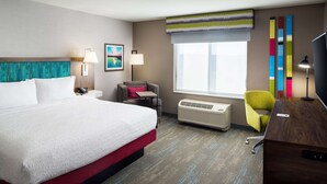A hotel room with a large bed, a desk, a chair, a window with blinds, a wall-mounted TV, and a painting. - Hampton Inn Kissimmee North (Kissimmee)