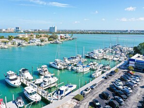 A marina with numerous boats docked, a parking area with cars, and a view of the cityscape in the background. - Bayside Condos Studio 23 Pool, Bay Views. Walk to Beach (Clearwater Beach)