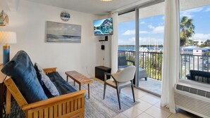 Sala de estar com sofá, televisão, pintura e vista para o porto de iates.