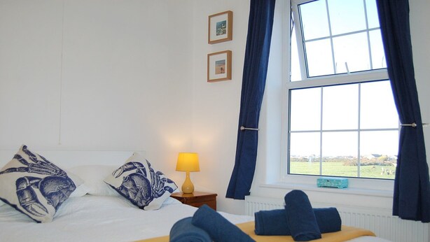 A hotel room with a bed, a window with curtains, a nightstand with a lamp, and a view of the outdoors. - Angorfa Family Holiday Home with Games Room (Tywyn)