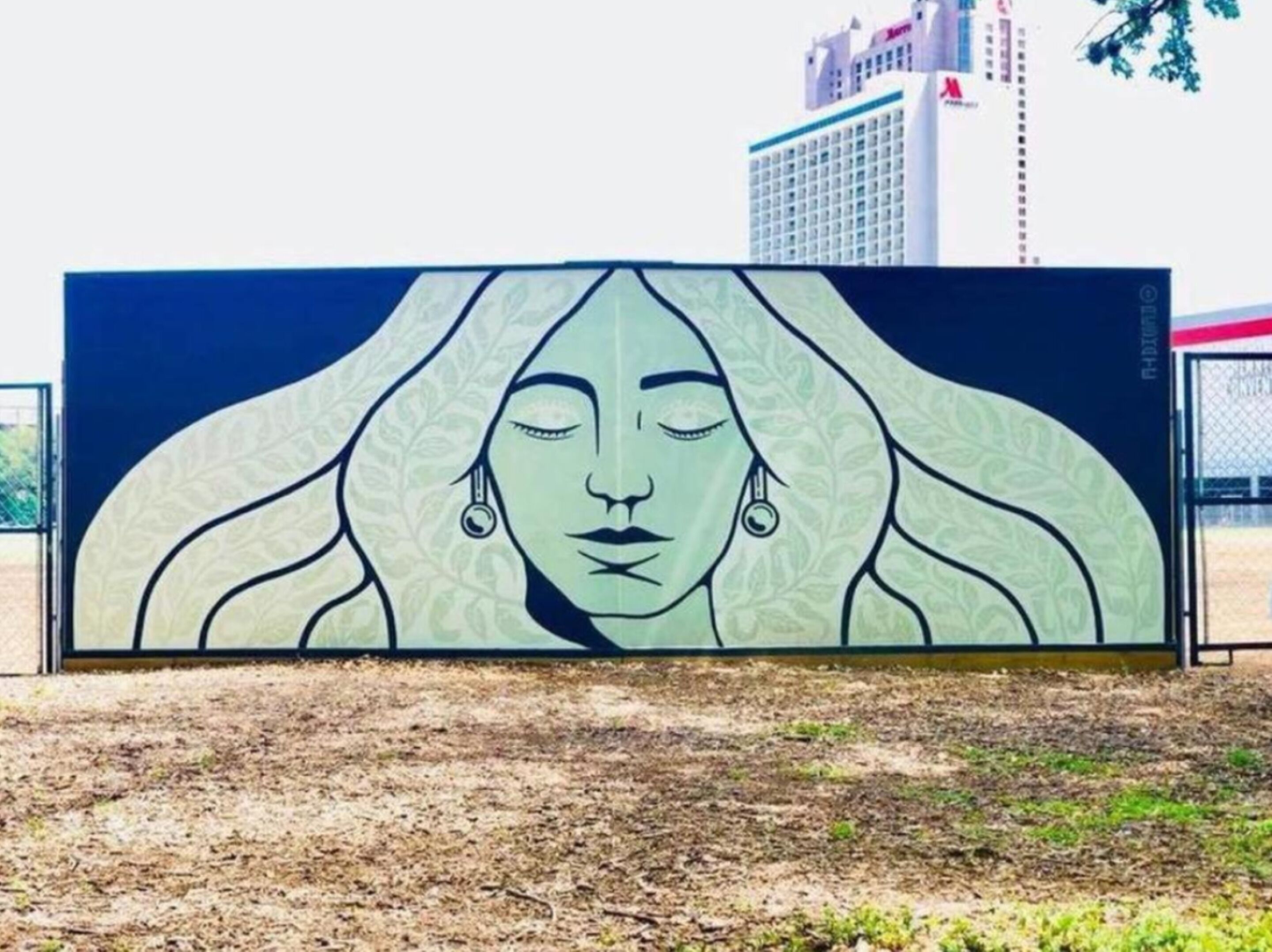 Une grande fresque extérieure représentant le visage d’une femme, encadrée par une clôture.