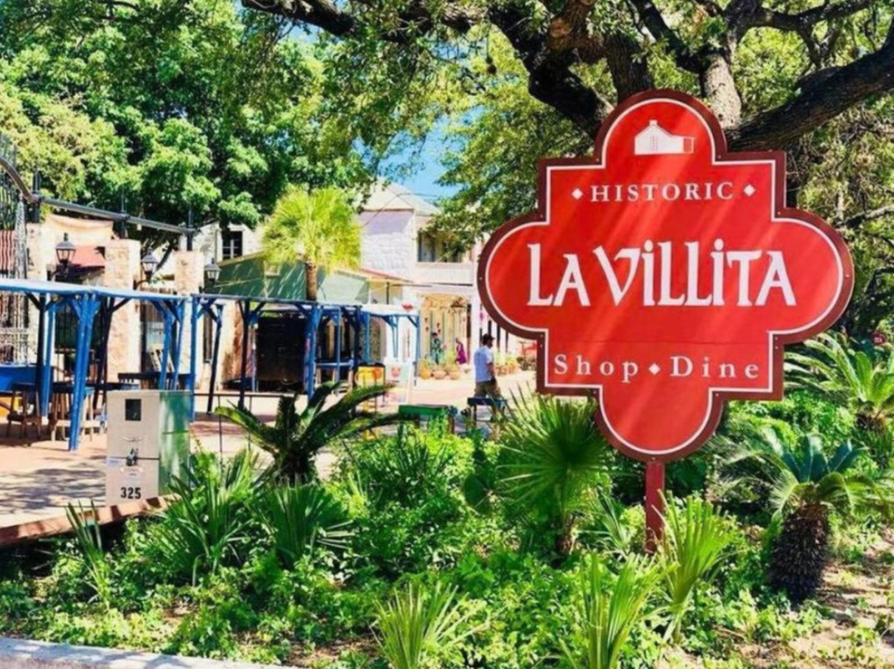 Un panneau rouge sur lequel on peut lire « LAVILLITA Shop & Dine » et « HISTORIQUE », entouré de verdure et de bâtiments.