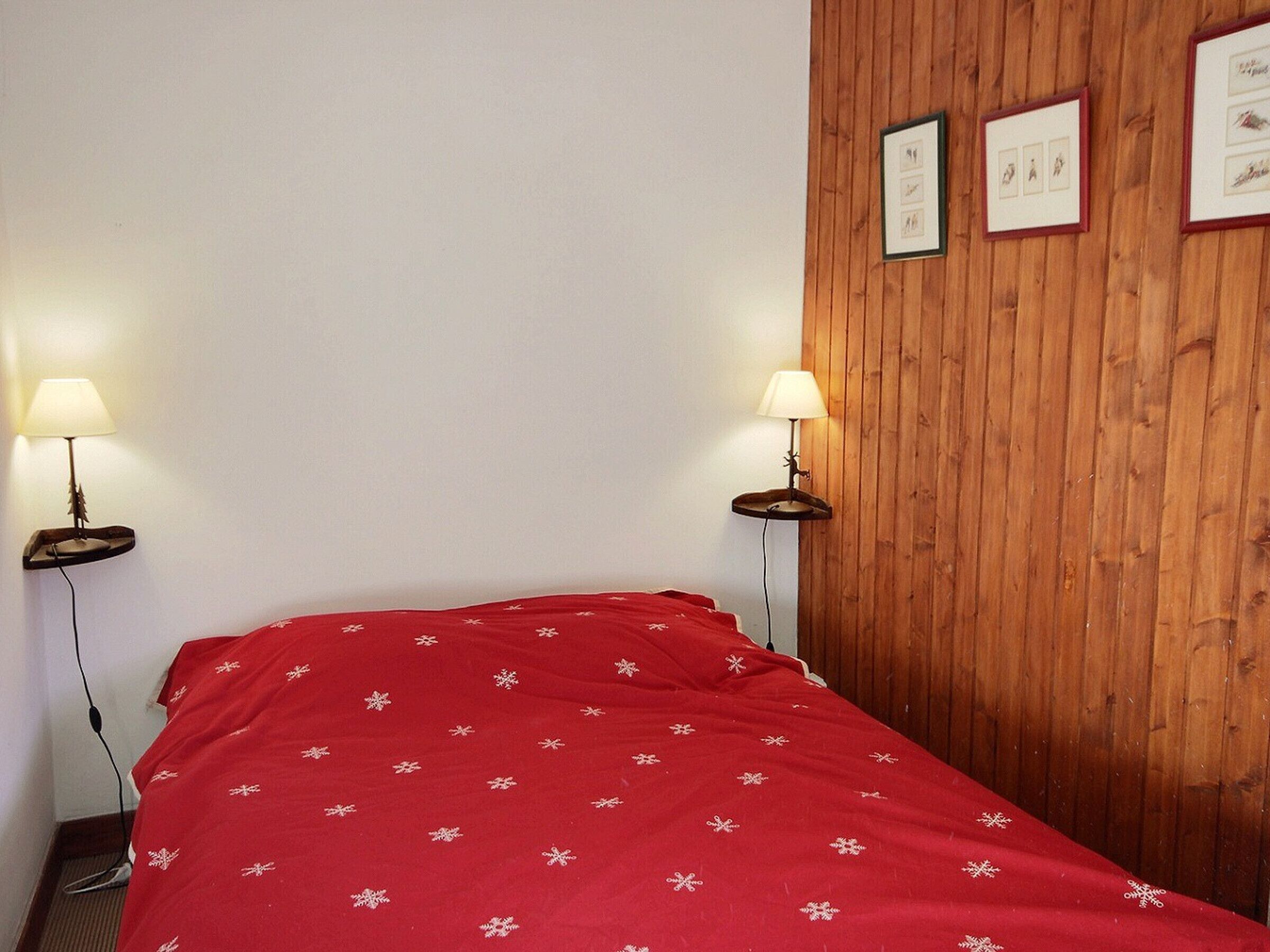 A room with a bed, two bedside lamps, a wooden panel wall, and framed pictures.
