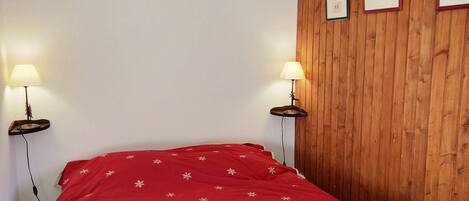 A room with a bed, two bedside lamps, a wooden panel wall, and framed pictures.