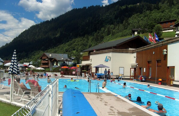 A swimming pool area with a mountain backdrop, surrounded by buildings with wooden facades.