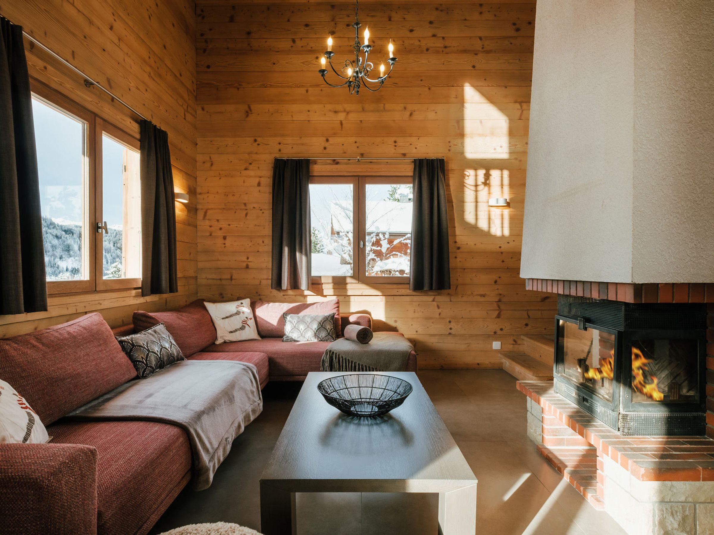 A cozy log cabin interior with a sofa, a table with a bowl, a fireplace, and large windows.