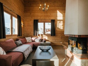 Een gezellig blokhutinterieur met een bank, een tafel met een kom, een open haard en grote ramen.