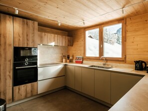 Een moderne keuken met houten kastjes, een Bosch oven, een magnetron en een raam met uitzicht op een besneeerd landschap.