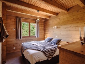 A wooden cabin bedroom with a bed, bedside table, and a window with curtains. - 4★ Chalet, 8 pers, cozy, near slopes, La Clusaz (La Clusaz)