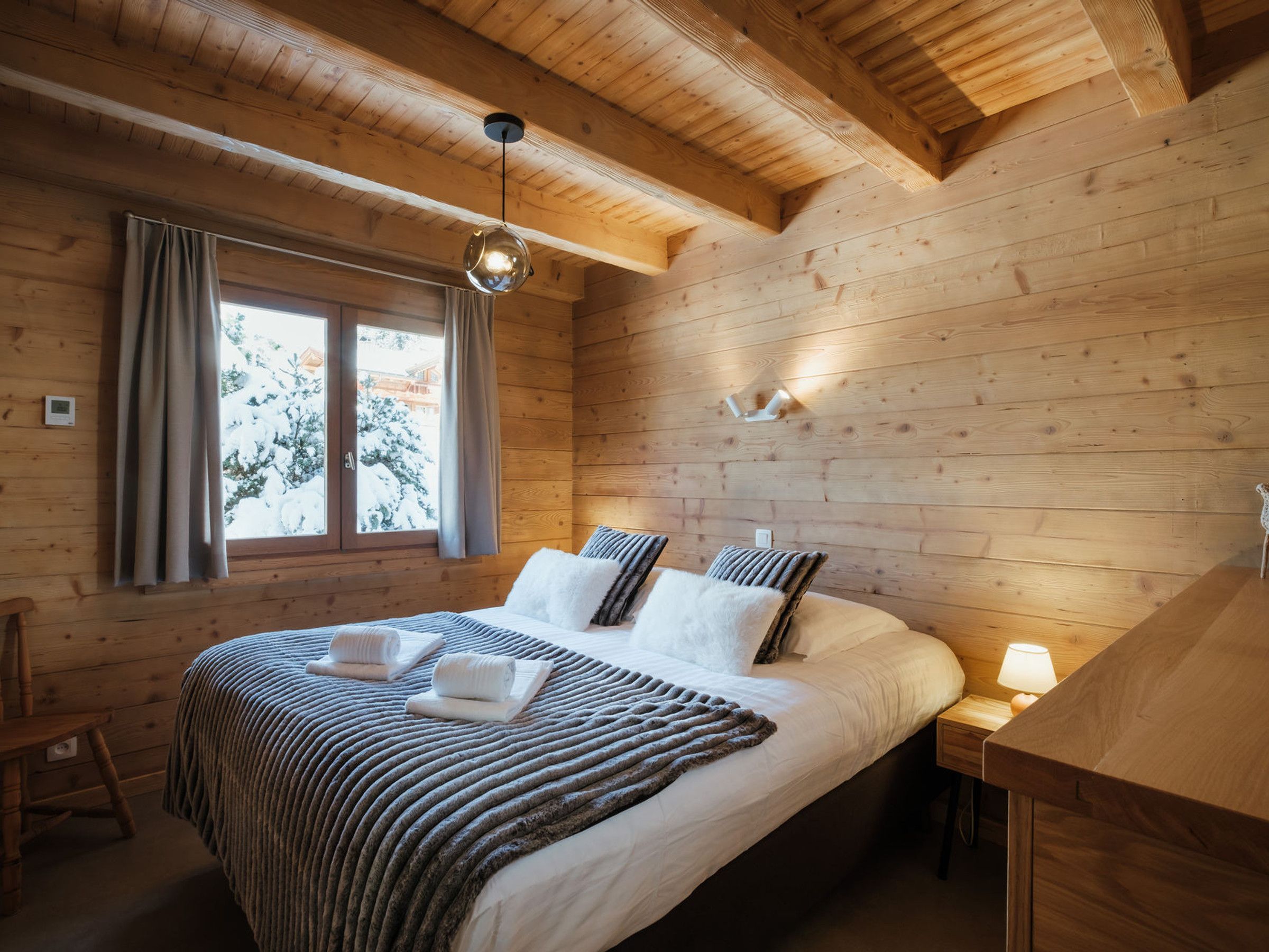 Un dormitori de cabana de fusta amb llit, finestra i lluminària penjant.