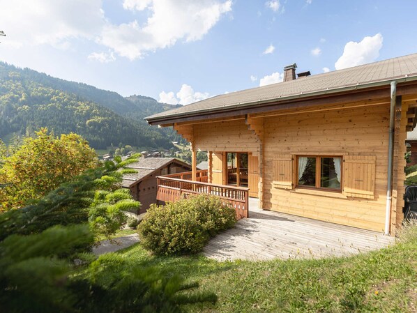 Une cabane en bois dotée d’un balcon, entourée de verdure et de montagnes.