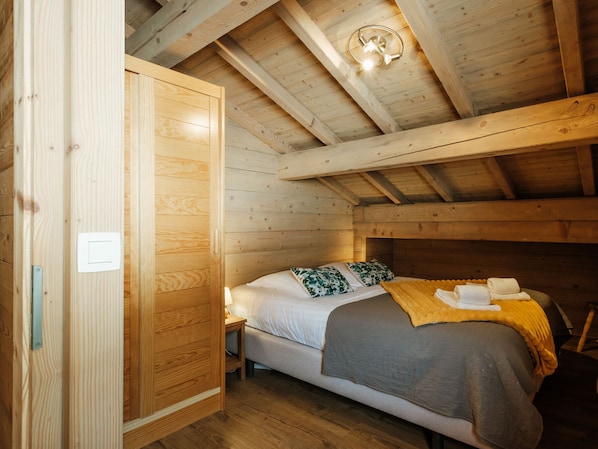 A wooden cabin bedroom with a bed, pillows, a bedside table, and a ceiling light fixture.