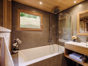 A modern bathroom with a glass-enclosed shower, a white bathtub, a wooden vanity, and a window with a view of greenery. - 4★ Chalet, 8 pers, cozy, near slopes, La Clusaz (La Clusaz)