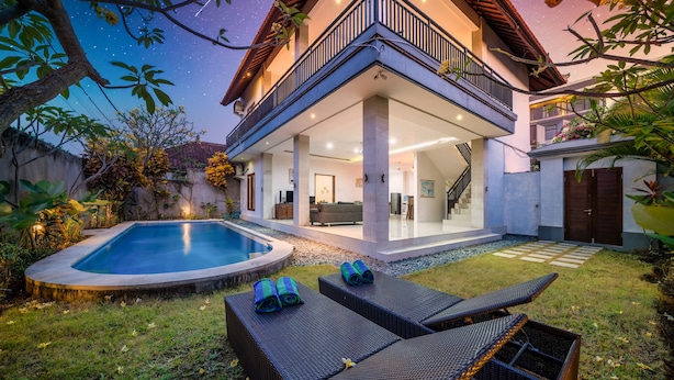Una casa de dos pisos con piscina, mobiliario exterior y balcón.