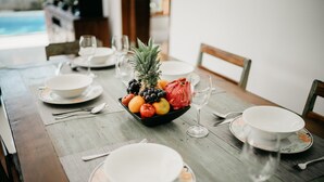 Una mesa de comedor con frutero, platos y copas de vino.
