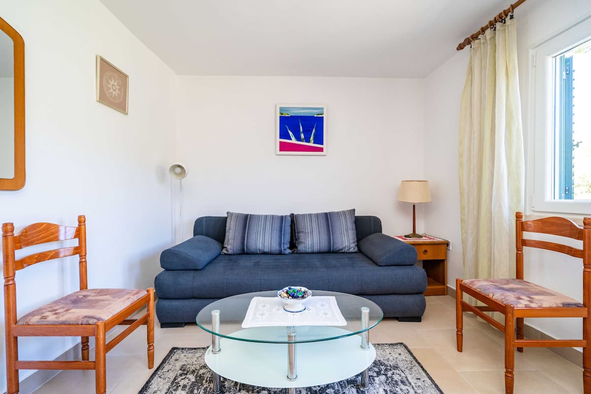 Un salon avec un canapé bleu, deux fauteuils en bois, une table basse en verre et un tableau encadré accroché au mur.