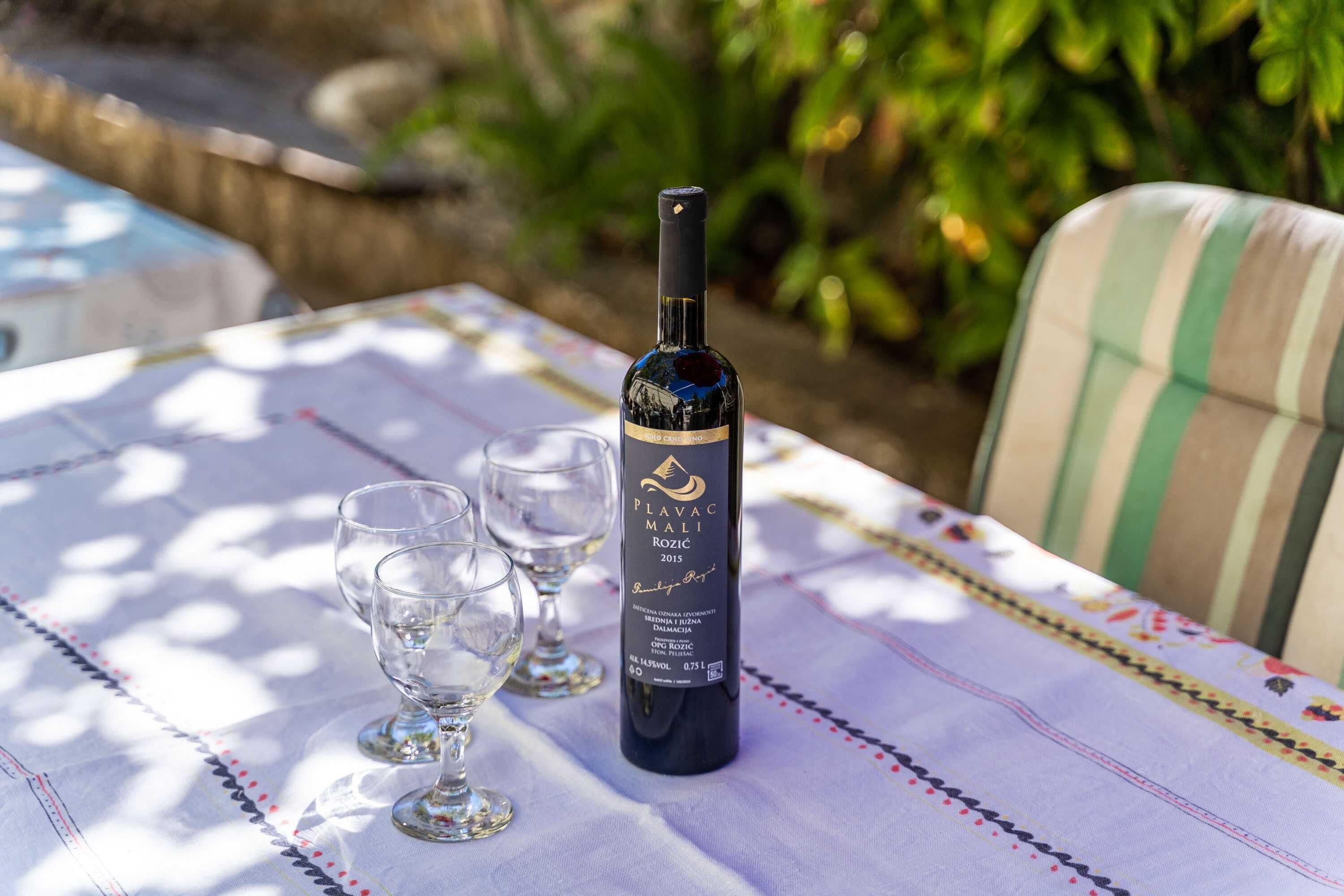 A bottle of Plavac Mali 2015 wine on a table with two glasses.