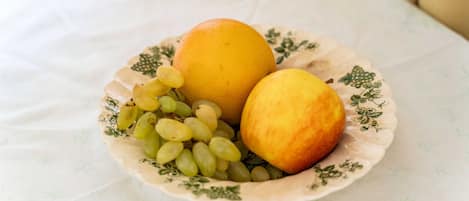 Un plato con una naranja, un melocotón y uvas sobre un mantel con estampado floral.
