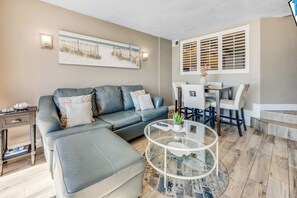 A modern living room with a grey sofa, a glass coffee table, and a dining area with a white table and chairs.