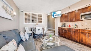 A modern living room with a gray sofa, a glass coffee table, and a dining area with white chairs. - Beach Cove condo with balcony & beach access (North Myrtle Beach)