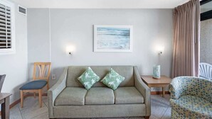 A living room with a sofa, two pillows, a chair, a small table, and a picture on the wall. - Beach Cove Resort condo, pool & hot tub (North Myrtle Beach)
