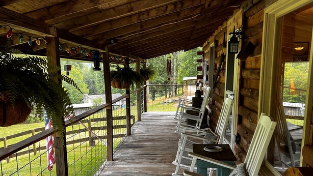 A covered porch with wooden flooring, white rocking chairs, and a metal railing. - Lovely cabin on 136acre, 13 Miles from North Asheville.  6 miles from BR Parkway (Weaverville)