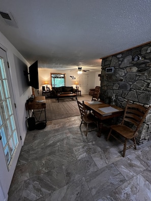 Relax in this inviting living space with a sofa, chairs, and dining table for four, plus a TV and ceiling fan.
