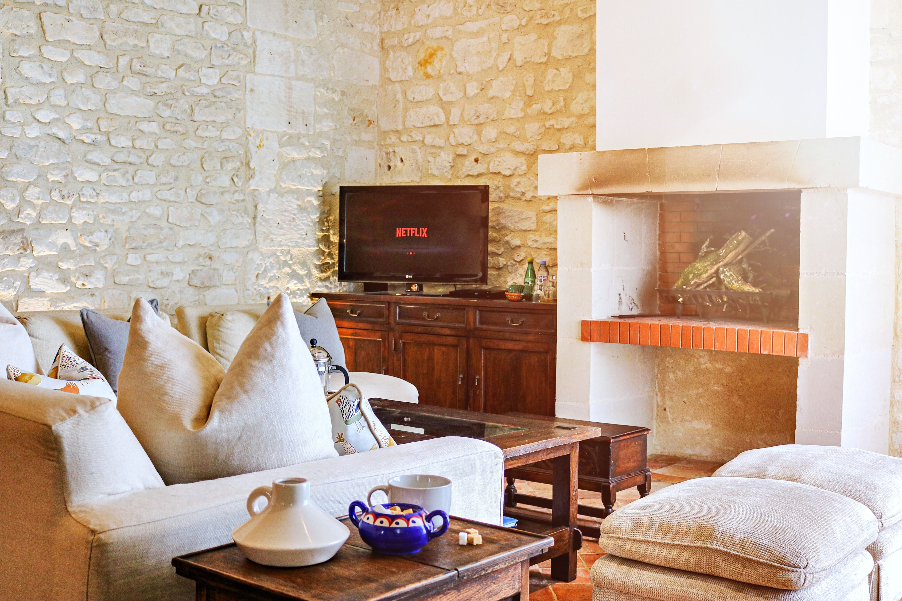 Un salon avec un mur en pierre, un téléviseur, une cheminée et un canapé avec des coussins.