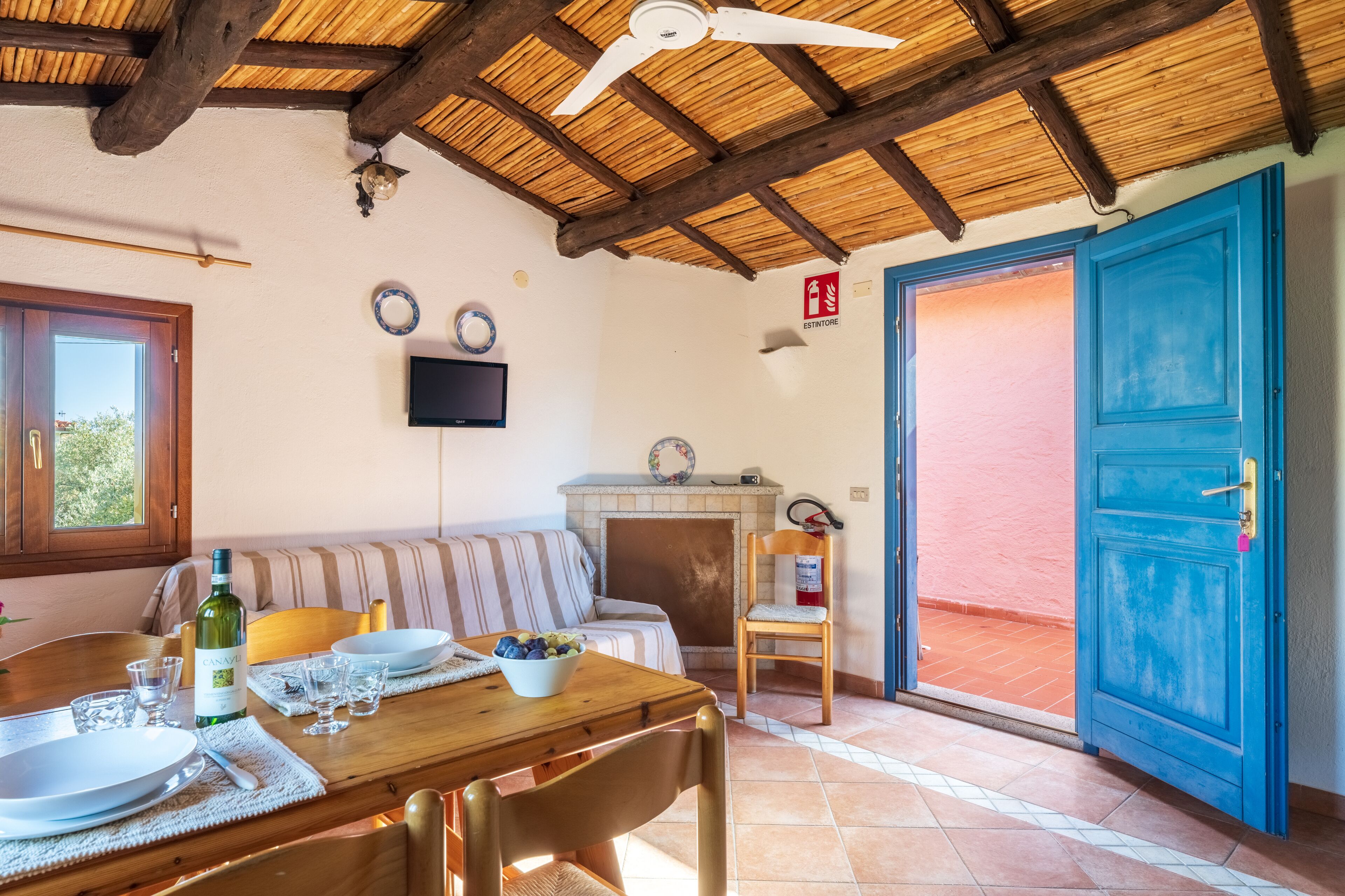 Un comedor con una mesa de madera dispuesta para dos personas, un sofá y un televisor montado en la pared.