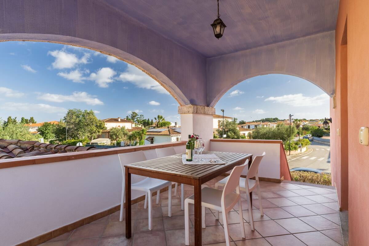 Uma varanda com mesa e cadeiras, uma garrafa de vinho e vista do bairro.