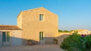 A stone building with a tiled roof, a small window, and a door. There are potted plants and a paved courtyard. - Baglio Cella, Basil annex in the Hyblean countryside (Modica)
