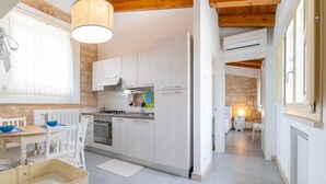 A modern kitchen with white cabinets, a stove, and a dining area with a table and chairs. - Baglio Cella, Basil annex in the Hyblean countryside (Modica)