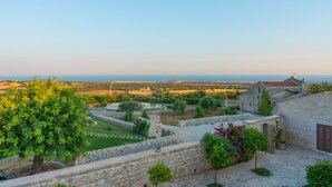 A stone courtyard with a view of the sea, surrounded by greenery and a stone wall. - Baglio Cella, Basil annex in the Hyblean countryside (Modica)