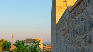 A stone wall with a paved walkway leading to a building with a tiled roof. - Baglio Cella, Basil annex in the Hyblean countryside (Modica)