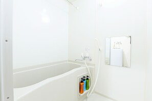 Une salle de bain blanche avec une baignoire, un miroir et un distributeur de savon fixé au mur.