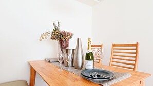 Une table de salle à manger en bois, avec une bouteille de champagne, deux verres à vin, un pichet en métal et un vase rempli de fleurs.