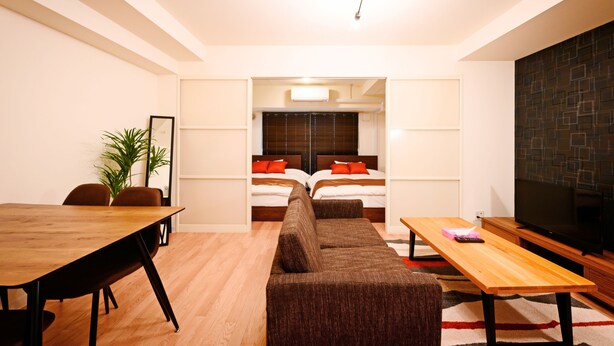 Une chambre d’hôtel moderne avec une table à manger en bois, un canapé, une télévision et un lit agrémenté d’oreillers rouges.